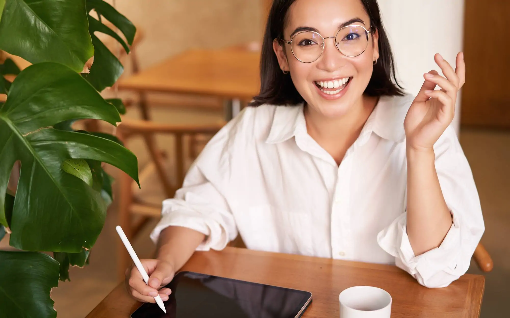 Mulher jovem sorridente com óculos usando um tablet, representando a satisfação com o tratamento de facetas de resina na clínica Ferdinand Odontologia, na Tijuca, Rio de Janeiro