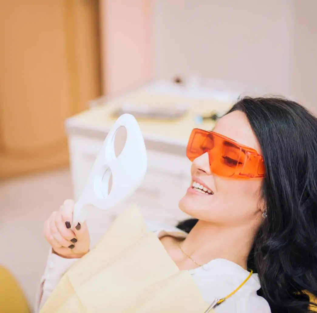 Paciente sorrindo ao espelho após colocar lentes de contato dental em porcelana na Ferdinand Odontologia, referência de dentista na Tijuca, RJ