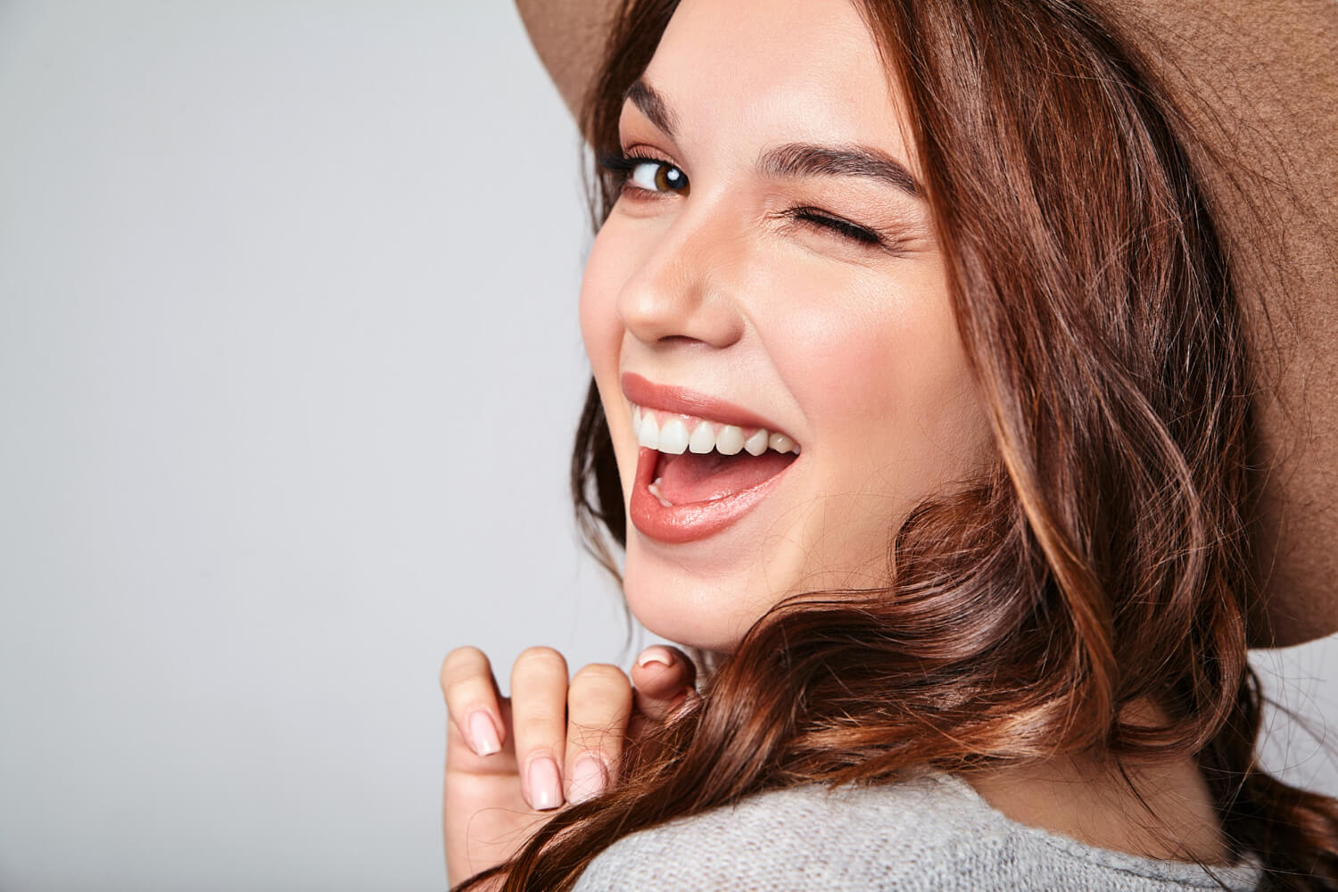 Mulher jovem de chapéu sorrindo e piscando, exibindo dentes perfeitamente alinhados após tratamento com ClearCorrect na Tijuca.