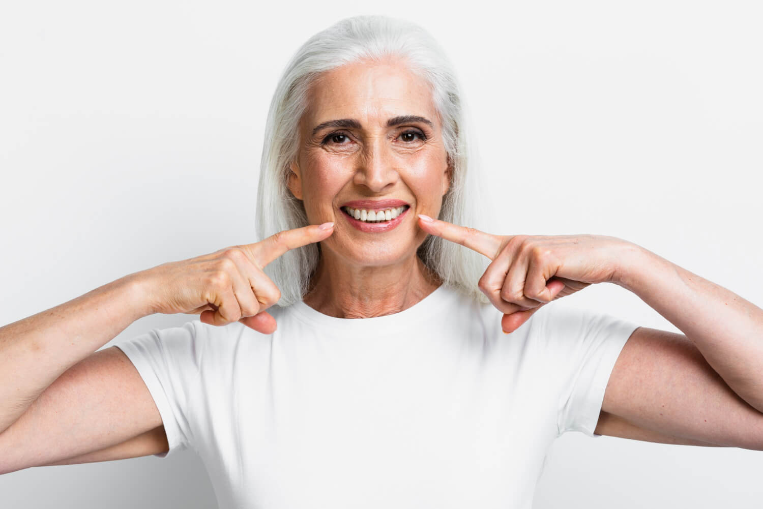 Senhora sorridente apontando para seus dentes perfeitos após tratamento de implante dentário na Clínica Ferdinand Odontologia na Tijuca.