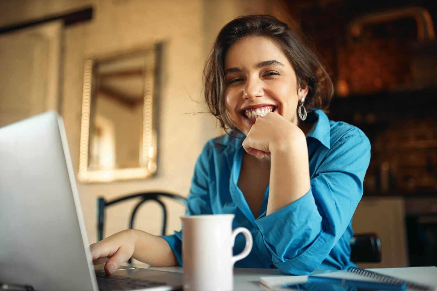 Jovem sorrindo em frente ao laptop com uma caneca, mostrando opções do que beber usando alinhadores Invisalign na Tijuca, Rio de Janeiro.